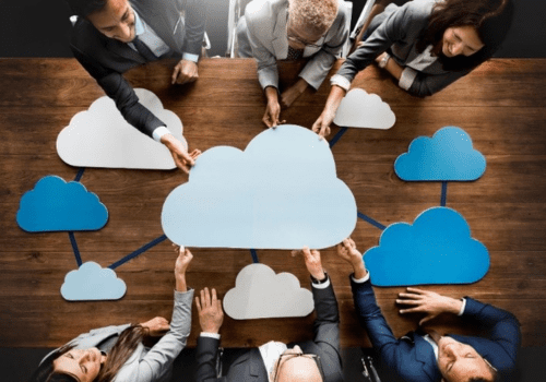 people in a board room sitting on either side of a table with cloud icons in the middle