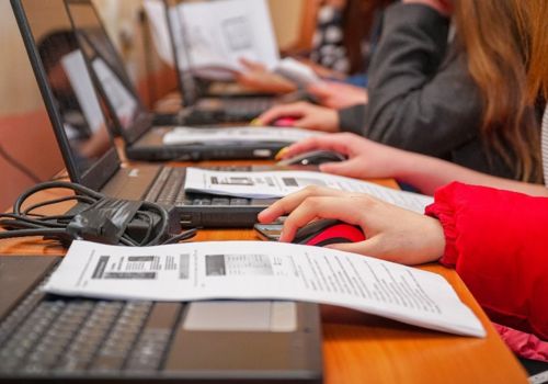 laptops with peopels hands visible and instruction handouts on each one